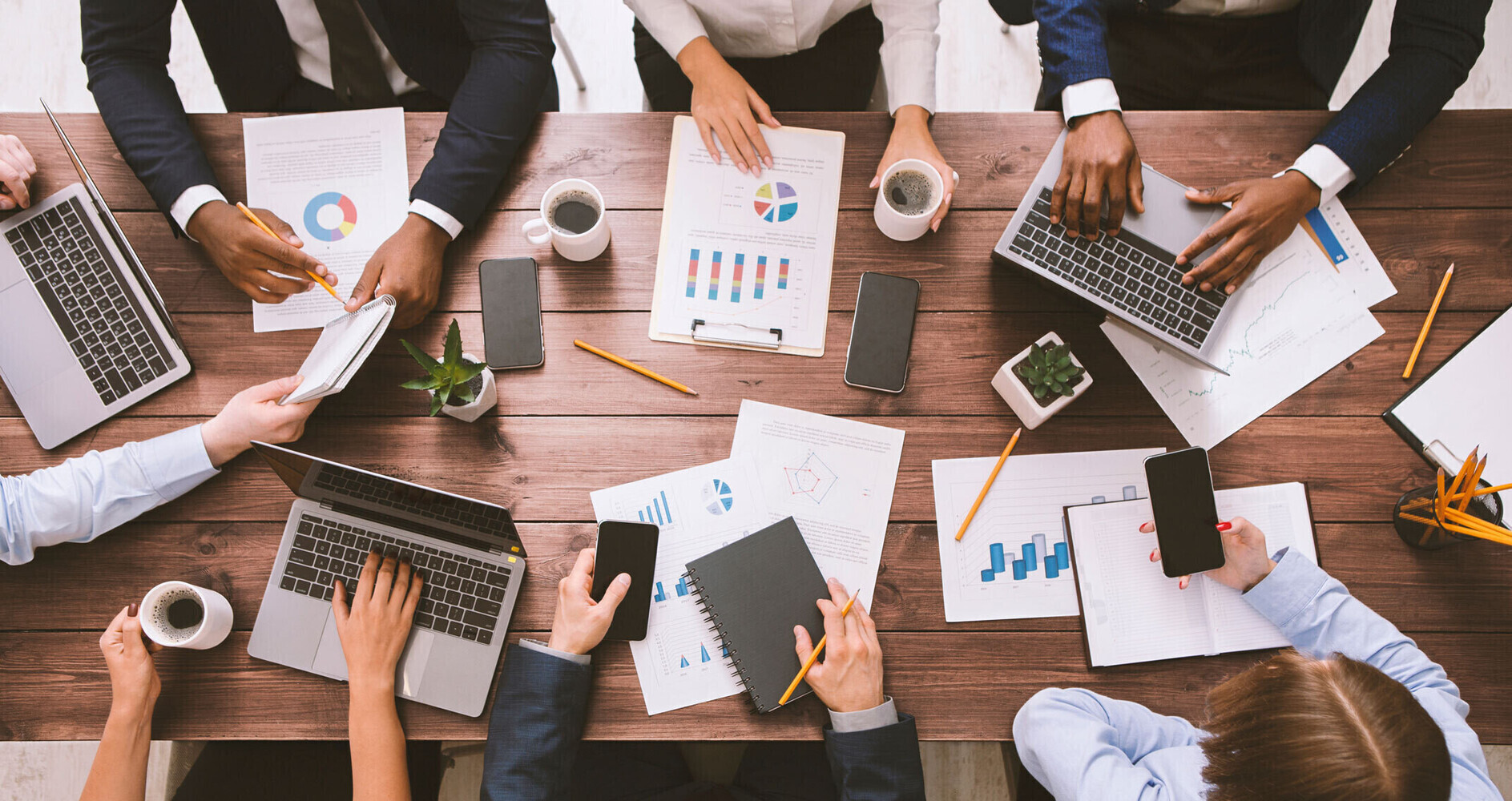 Group of people sitting around a table, discussing over charts and papers.
